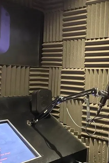 Sarea's recording booth: a microphone on a boom arm, a studio monitor and a script screen, surrounded by acoustic foam